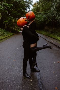 a man and woman dressed up as witches kissing in the street with pumpkins on their heads