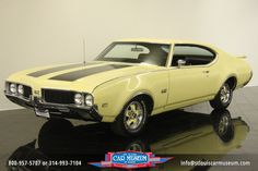 a yellow muscle car sitting on top of a shiny black floor next to a white wall