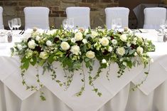 the table is set with white flowers and greenery for an elegant wedding reception in front of a brick wall