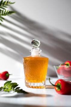 a glass bottle filled with liquid sitting on top of a table next to red peppers