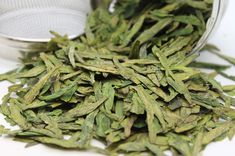 a pile of green tea leaves sitting on top of a white table next to a metal strainer