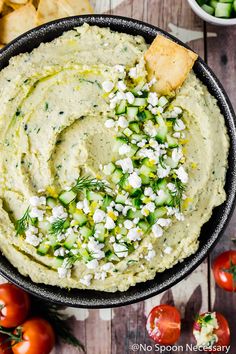 a black bowl filled with hummus, cucumber and tomatoes next to chips