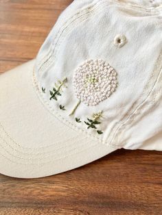 a white hat with embroidered flowers on it sitting on top of a wooden table next to a pair of scissors