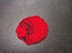 a red and black embroidered patch with a woman's head in the center on a leather surface