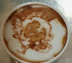 a white cup filled with liquid on top of a metal table covered in brown and white designs