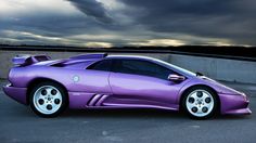 a purple sports car is parked in a parking lot with dark clouds behind it,