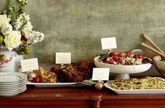 a table topped with plates and bowls filled with food next to a vase full of flowers