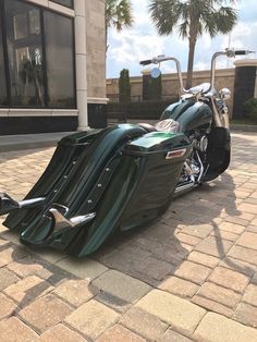 a green motorcycle parked on the side of a road next to a building with palm trees