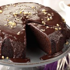 a chocolate cake with one slice cut out and topped with chopped nuts on a silver platter