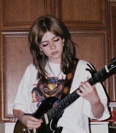 a young woman playing an electric guitar in a kitchen with wood paneling on the walls