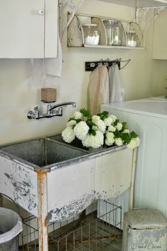 an old sink with some flowers in it and other items on the wall behind it