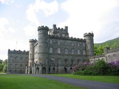 an old castle with lots of green grass and purple flowers on the front lawn area