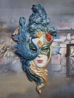 a blue mask with feathers on it and a red flower in the center is sitting next to a brick wall