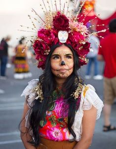 a woman with face paint and flowers on her head is standing in the middle of a street