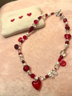 a red and white necklace with hearts on it, next to a small pouch that says i love you