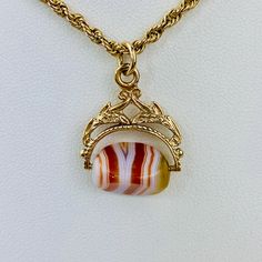 "This is a beautiful Victorian style Swivel Fob Seal / Pendant in 9K / 9ct yellow gold. The spinning fob pendant features hand carved floral gold design and a triangle shaped banded agate with vibrant white, red/orange, and yellow colors. The fob measures 0.87\" (22.3mm) high including bail without split ring and 0.76\" (19.4mm) wide at it is widest point. It is fully hallmarked for Birmingham Assay, 9ct gold, and year letter for 1977. It weighs 3.862 grams. All of our listings come in a box rea Yellow Gold Oval Agate Jewelry, Oval Agate Yellow Gold Jewelry, Oval Yellow Gold Agate Jewelry, Classic Formal Agate Jewelry, Gold Agate Hallmarked Jewelry, Formal Agate Jewelry With Engraving, Formal Engraved Agate Jewelry, Antique Gold Agate Jewelry, Vintage Gold Agate Jewelry