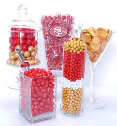 three clear vases filled with candy and gold coins next to each other on a white surface