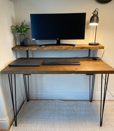 a desk with a computer on it in front of a wall mounted monitor and keyboard