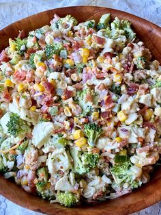 a wooden bowl filled with corn and broccoli salad on top of a table