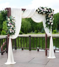 an outdoor wedding ceremony setup with white drapes and flowers on the arch, along with greenery