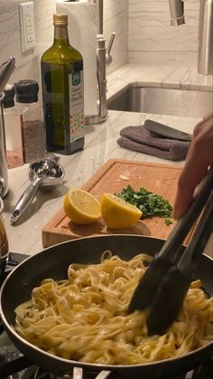 a person is cooking pasta in a pan on the kitchen counter with lemons and parsley