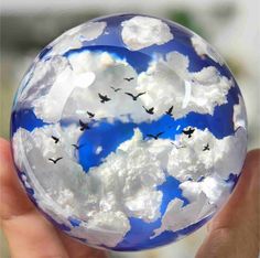 a hand holding a glass ball with clouds and birds in it