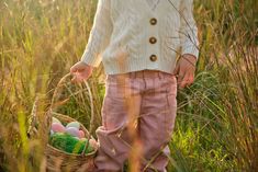 In this sweet Easter-themed visual, a child carries an Easter basket full of decorated Easter eggs through a spring meadow. It expresses the innocent joy of an egg hunt on Easter morning. Decorated Easter Eggs, Spring Meadow, An Egg, White Sweaters