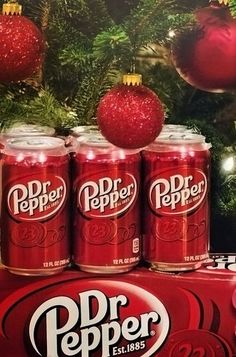 three cans of dr pepper are sitting in front of a christmas tree