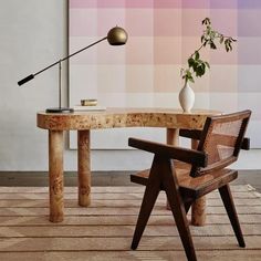 a table with a chair, lamp and vase on it in front of a colorful wall