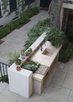 an outdoor bench with plants on it in front of a tree and walkway leading to a building