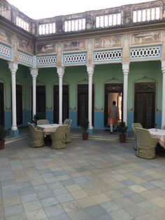 an outdoor courtyard with tables and chairs in the center, surrounded by pillars and arches