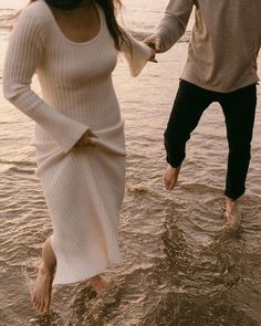 a man and woman are walking in the water holding each other's hands as they walk