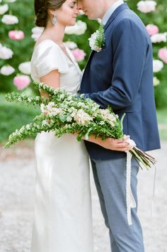 a bride and groom standing in front of pink flowers with greenery on their arms