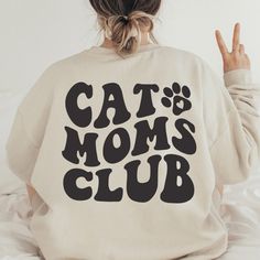 a woman sitting on top of a bed wearing a sweatshirt that says cat mom's club