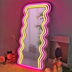 a pink and yellow mirror sitting on top of a wooden floor next to flowers in vases