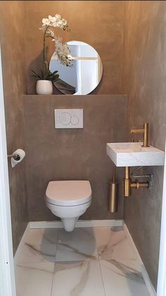 a white toilet sitting in a bathroom next to a sink under a mirror and a vase with flowers