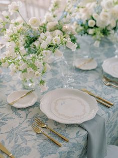 the table is set with white flowers and gold place settings