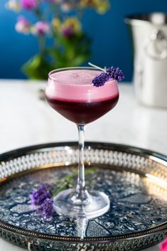 a purple drink sitting on top of a metal tray next to a vase with flowers