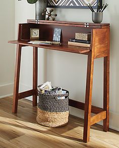 a wooden table with a basket underneath it and a painting on the wall behind it