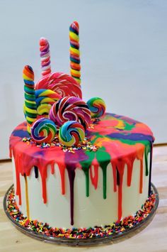 a multicolored birthday cake with candy and lollipops on the top