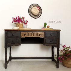 an old desk with flowers on it and a hat hanging from the wall behind it