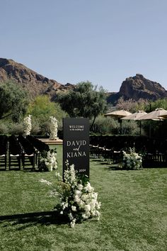 an outdoor ceremony setup with flowers and greenery on the grass in front of mountains