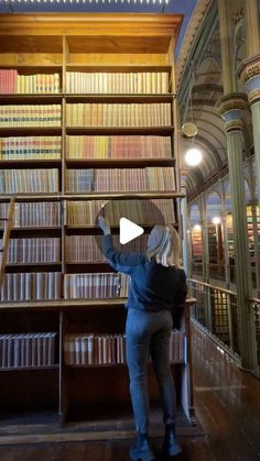 a woman standing in front of a large book shelf filled with lots of books on top of wooden floors