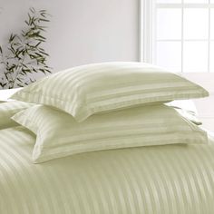 three pillows stacked on top of each other in front of a bed with white sheets