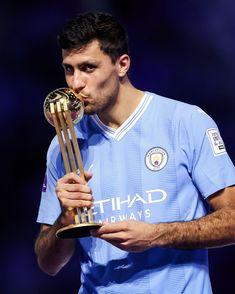 a man holding a trophy in his right hand and looking at it while wearing a blue shirt