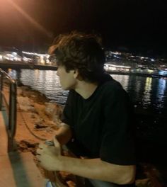 a young man sitting on the edge of a pier at night with his cell phone in his hand