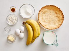 ingredients to make an apple pie laid out on a white counter top, including bananas, eggs and flour