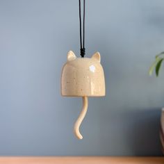 a cat shaped ceramic light hanging from a black cord on a wooden table next to a potted plant