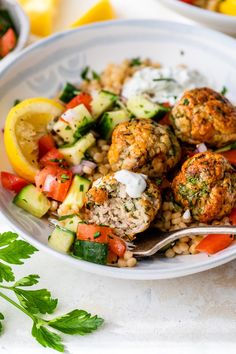 a white plate topped with meatballs and veggies next to lemon wedges