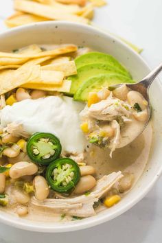 a white bowl filled with chicken, beans and avocado next to some tortilla chips